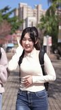 A vertical slow-motion video of two young Taiwanese female college students walking happily while talking on a university campus in Taipei, Taiwan