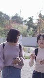 A vertical slow-motion video of two young Taiwanese female college students walking happily while talking on a university campus in Taipei, Taiwan