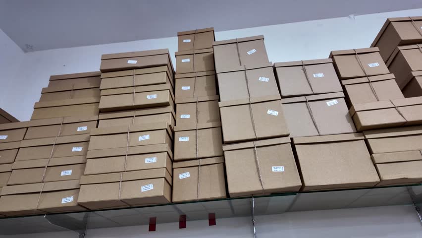 Stack of various cardboard boxes on a hanging rack in a packaging shop. Pile of carton giftbox with natural rope straps. Royalty-Free Stock Footage #3449969607