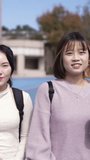 A vertical video of two young Taiwanese female college students walking happily while talking on a university campus in Taipei, Taiwan