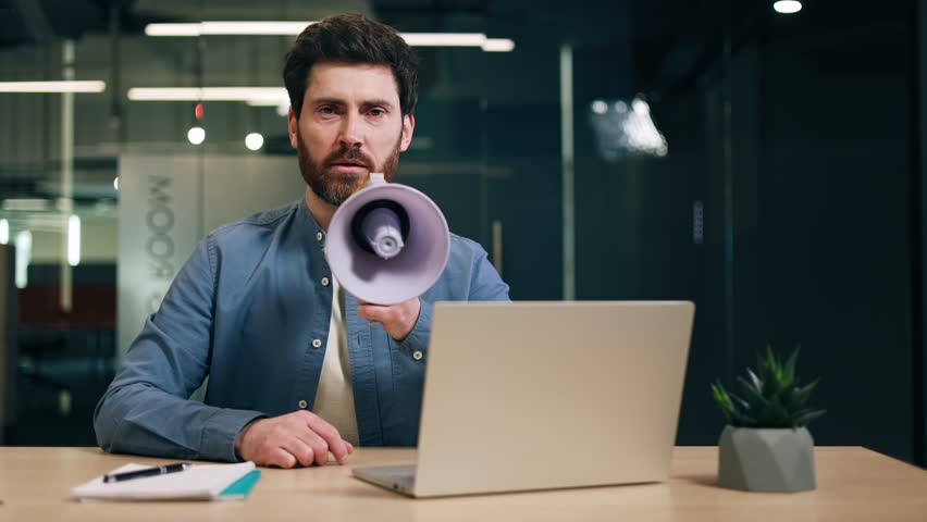 Bossy entrepreneur in casual outfit expressing negative emotions while yelling through bullhorn in workspace with pc. Cynical chef showing disrespect for employees at company office with glassy walls. Royalty-Free Stock Footage #3449990811