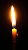 A funeral candle burning in total darkness. The concept of religion, mourning and memory. Close-up of a burning candle. Vertical video for shorts.
