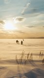 Winter fishermen return to shore from fishing at sunset. A strong wind has risen, gusts of wind are blowing away the snow. Vertical video for shorts.