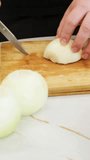 Close-up of male hands cutting onions with a knife on a chopping board. Onions are cut into half rings for marinating fresh meat. Vertical video for shorts.