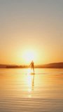 A young man is sailing through a quiet place on a SUP board at sunset. A beautiful golden sunset. Active recreation of a person in nature. Vertical video for shorts.