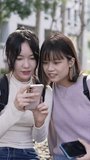 Vertical video of two young Taiwanese female college students sitting happily talking on a university campus in Taipei, Taiwan