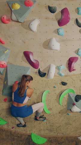 Vertical Portrait of Athletic Female Rock Climber Practicing Solo Climbing on Bouldering Wall in a Gym. Female Exercising at Indoor Fitness Facility, Doing Extreme Sport Lifestyle Training