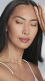 Female Beauty Vertical Portrait. Beautiful Asian Happy Brunette Woman Posing, Touching Her Face with Natural, Healthy Skin. Wellness and Skincare Concept on Soft Isolated Background. Close Up.