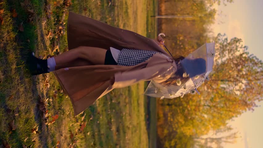 A girl spins with an umbrella in an autumn park. Joyful autumn scene with colorful foliage, rain protection, transparent umbrella, weather forecast
