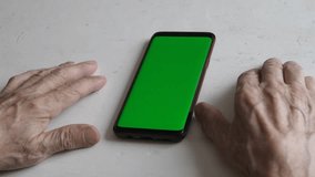 hands of an elderly man on the table. Green chromakey on the smartphone screen for content. Exploring new horizons:, pensioner and green chromakey on the gadget