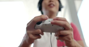 Teenage Asian boy focused on gaming at home. He's intensely engaged with his video game controller, indicating leisure time, slow motion.