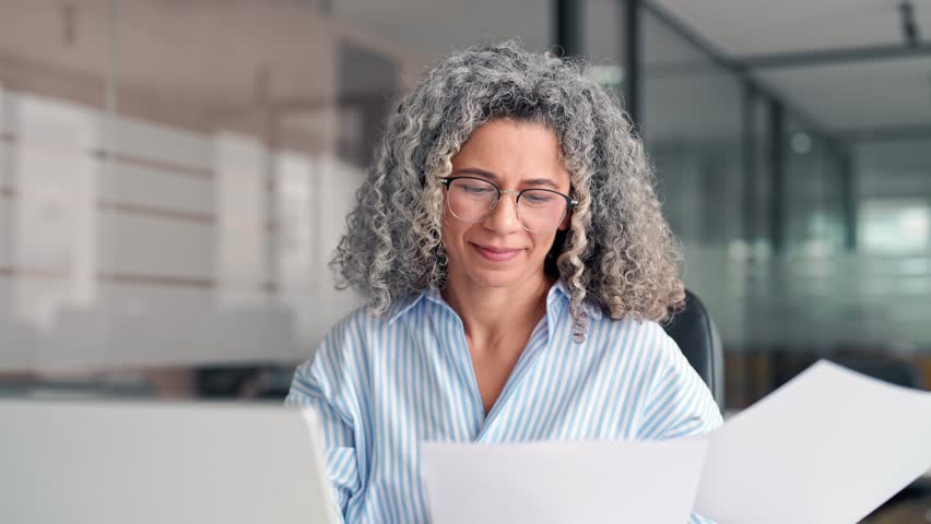Busy middle aged business woman working in office with laptop reading document. Mature professional hr manager, notary holding paper finance report sitting at desk in office. Consultancy. Royalty-Free Stock Footage #3450149771