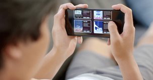 Teenage Asian boy browses a video streaming service on a smartphone at home. Engrossed in the digital world, the student explores a variety of apps and media, slow motion.