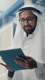 Vertical Screen: Muslim Businessman in Traditional White Kandura Riding Glass Elevator to Office in Modern Business Center. Man Using Tablet Computer. Saudi, Emirati, Arab Businessman Concept.