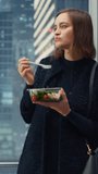 Vertical Screen: Confident Young Female Riding Glass Elevator to Office in Modern Business Center and Eating Healthy Salad with Vegetables. Happy Manager Preparing for Productive Day at Work.