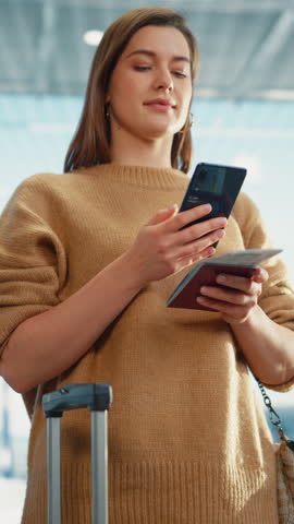 Vertical Screen. Airport Terminal: Happy Traveling Caucasian Woman Waiting at Flight Gates for Plane Boarding, Uses Mobile Smartphone, Checking Trip Destination on Internet. Smiling Female on a Trip