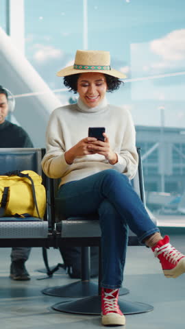 Vertical Screen. Airport Terminal: Happy Black Woman Waits for Flight, Uses Smartphone, Browse Internet, Post on Social Media, Online Shopping. Traveling African American Female in a Boarding Lounge Royalty-Free Stock Footage #3450194169
