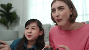 Girl winning game while caucasian mom clapping hands to celebrate successful achievement while sitting at living room. Attractive mother and daughter spend time together while hold joystick. Pedagogy.
