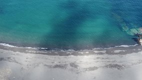 Camera moving sideways along a black sandy beach in Patagonia clear blue sea and small waves lapping the beach