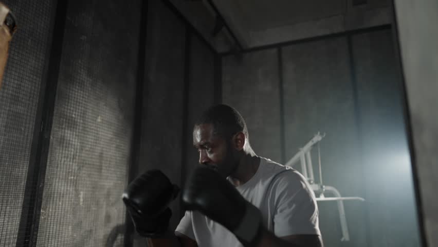 Boxer training hitting punching bag. African american sweated sportsman practicing punches in gym wearing boxing gloves. Workout, martial art, training, athletic sport, kickboxing, fighting concept. Royalty-Free Stock Footage #3450279055