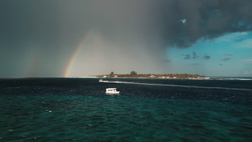 Surfing spot with surfers riding the waves during upcoming rain with rainbow on the horizon. The Maldives
