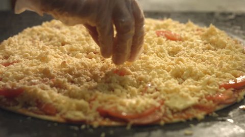 Cooking of pizza. 3 Shots. Slow motion.
1. Female hands sprinkle cheese pizza. Close-up.
2. Female hands spread cheese on pizza. Top view.
3. The pan with pizza is placed in the oven. 