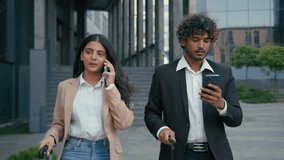 Two business coworkers partners Arabian businesswoman walking in city airport terminal talking mobile phone call Indian businessman browsing typing smartphone with luggage baggage corporate travel - Powered by Shutterstock - Get 15% off with code: PIKWIZARD15