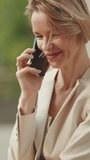 VERTICAL VIDEO, Happy businesswoman with blond hair talking on cellphone, good deal, success