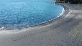 Small waves breaking on black beach in Chile Patagonia with green forest