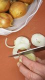 Vertical video – Closeup overhead shot of a man’s hands slicing a raw white onion on a chopping board, with a steel knife, next to a bag of onions.