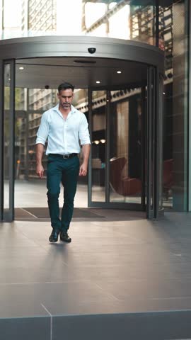 Mature businessman with neat beard wearing white shirt leaves the office in the financial district in the city