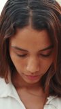 VERTICAL VIDEO: Clouse-up, beautiful girl with brown long hair, tanned skin raises her head and looks straight into the camera. Young women serious look at camera open and confident
