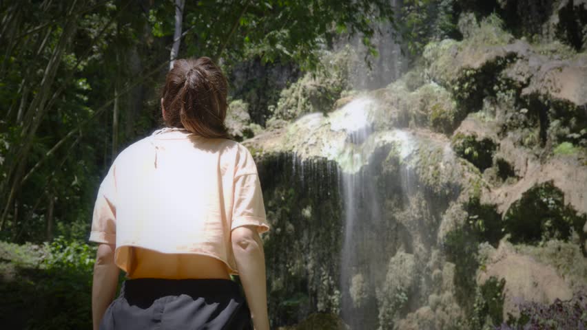 Woman gazing at the Tumalog Falls in Philippines, surrounded by lush greenery