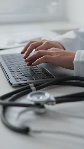 Young female doctor working on her laptop in clinic recording patients' medical data A doctor with a smile consults a patient online, using innovative technologies to provide quality medical care. Royalty-Free Stock Footage #3450408255