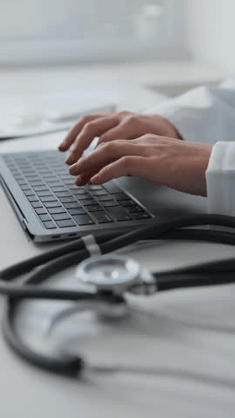 Young female doctor working on her laptop in clinic recording patients' medical data A doctor with a smile consults a patient online, using innovative technologies to provide quality medical care.: stockvideo