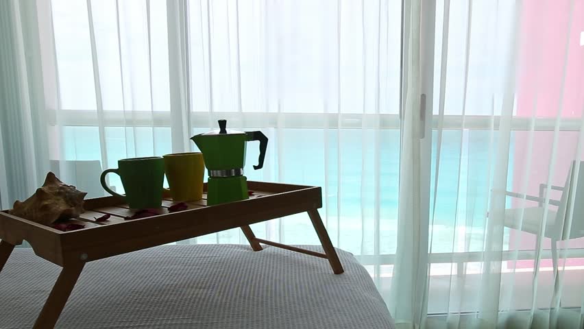Breakfast wooden tray with coffee percolator and cups on bed at hotel room with ocean view. Caribbean vacation. Nobody