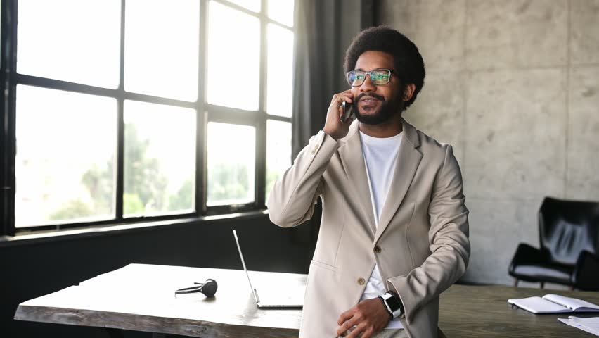 Young businessman is engaging happily on a phone call captured against the serene backdrop of an urban office. The photograph encapsulates a moment of pleasant business communication Royalty-Free Stock Footage #3450414411