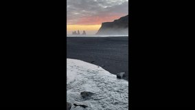 Sunset on Black Sand Beach Vik, Iceland. Reynisdrangar cliffs and sea stacks. Views of the cliffs and stone stack from Vik near Ring Road. Vertical video.