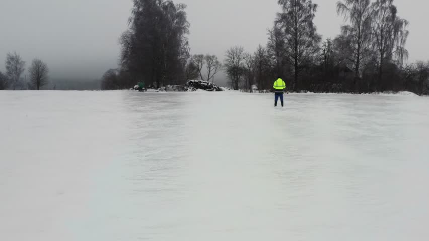 Flying above frozen field with ice layer, person in green jacket stand