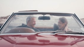 View through windshield of retired senior couple on vacation sitting in classic convertible sports car at beach watching morning sunrise and drinking coffee on road trip - shot in slow motion - Powered by Shutterstock - Get 15% off with code: PIKWIZARD15