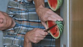 Vertical video. Young man cutting fresh red watermelon on a chopping board on slices indoors, slow motion