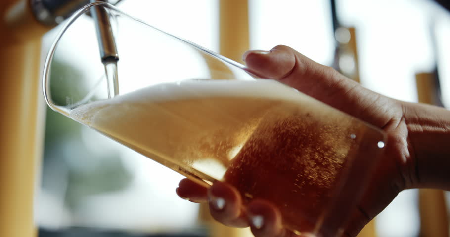 Female bartender filling beer glass from tap. Bubbly and foaming drink