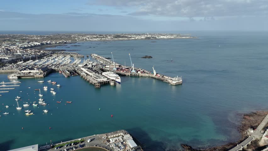 St Peter Port Guernsey flight over ferry terminal with ferry in dock, commercial dock with cranes with QE II Marina in background and views over Belle Greve Bay on bright sunny day Royalty-Free Stock Footage #3450517377