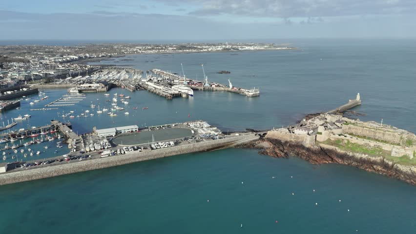 St Peter Port Guernsey flight towards ferry terminal with ferry in dock,over Havelet Bay, Castle Breakwater and marinas with views over Belle Greve Bay on bright sunny day with clear sea and blue sky Royalty-Free Stock Footage #3450517841