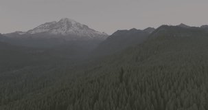 Ungraded wide-angle aerial drone footage of Mount Rainier at dusk as the last remaining sunlight of the day illuminates the sky above Washington State in a soft, warm glow.