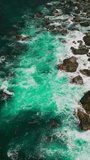 Turquoise water splashing by the stones at the shore. Rocky coastline of California with white waves splashing by. Vertical video.