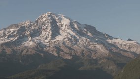 Ungraded aerial closeup footage of Mount Rainier under hazy blue sky on a bright, sunny afternoon in Washington State.
