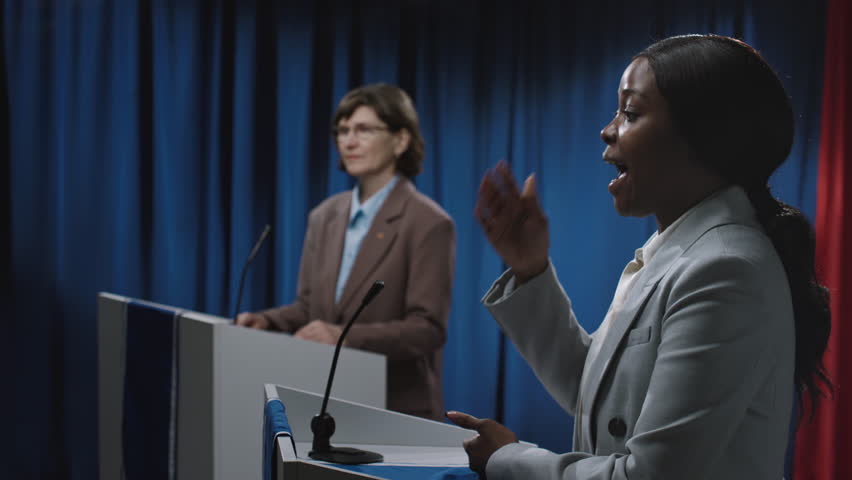 Medium close-up side shot of agitated young African American female politician giving angry speech at election debate, blaming economic crisis on opponents party, who is trying to defend herself Royalty-Free Stock Footage #3450573277