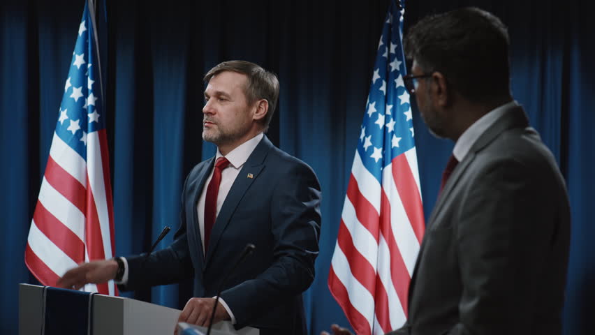 Medium shot of mature Caucasian male candidate running for election presenting his economic and social policy at public debate, and black male adversary interrupting and reproaching him Royalty-Free Stock Footage #3450575389