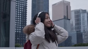 Happy asian female student listens to music on wireless headphones outside in Guangzhou city